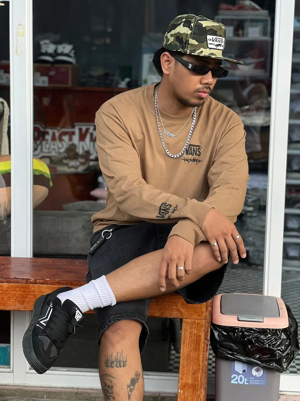 A person wearing a Vans cap, tan long-sleeve shirt, and black sneakers outside the store.